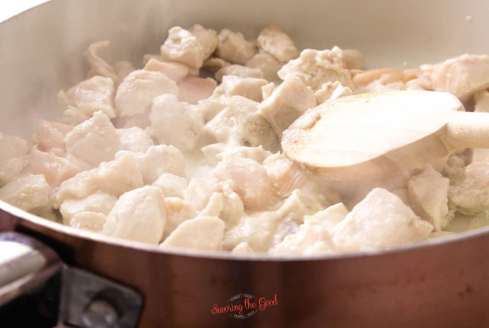 chicken taking on white color while cooking in a pan.