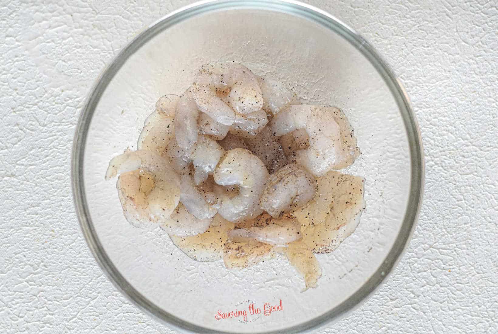 raw shrimp seasoned in a clear bowl.