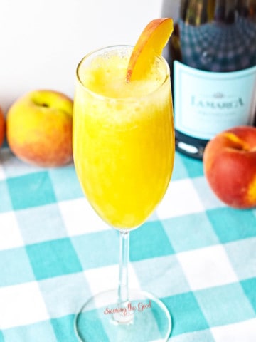 peach Bellini in a champagne glass on a teal gingham cloth.