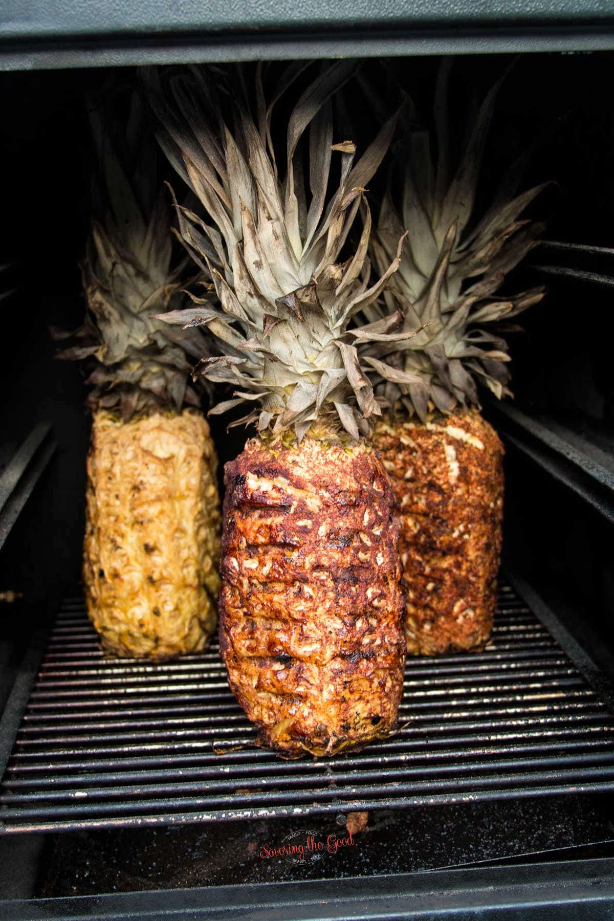 3 Smoked Pineapples with different seasonings on them in a smoker box, pineapple tops still in tact.