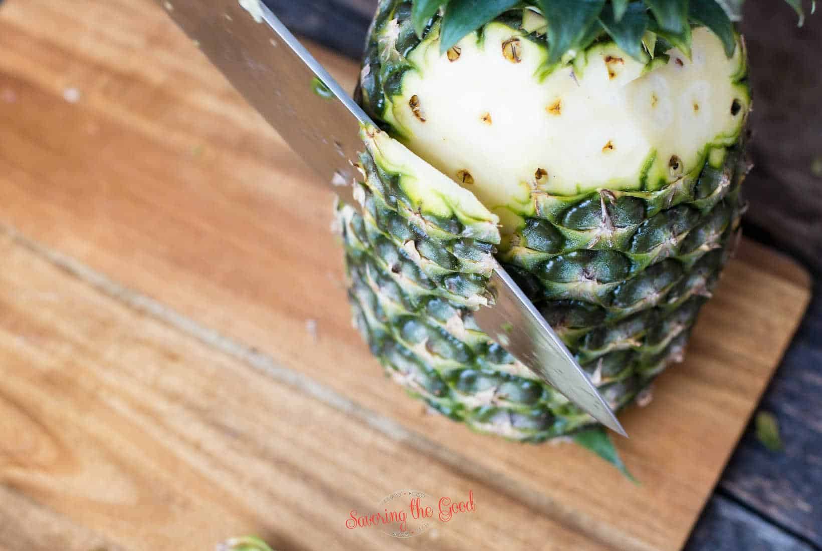 Chef knife cutting the outside of a pineapple off.