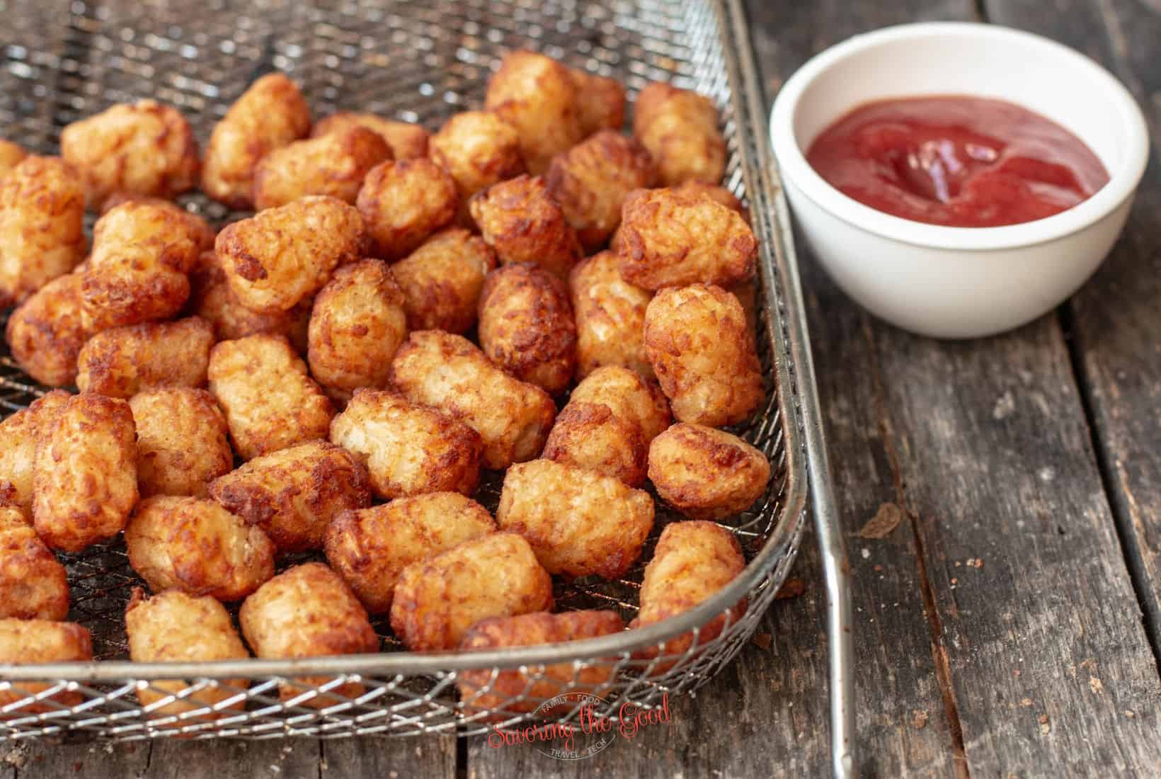 air fryer oven basket with cooked tots with a side of ketchup.