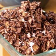 A glass dish filled with a mixture of chocolate-covered cereal pieces and melted marshmallows, reminiscent of golden graham s'mores.