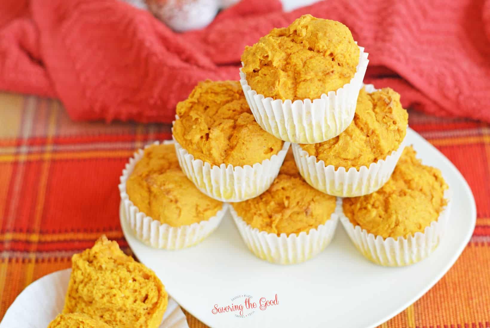 horizontal image of Pumpkin Muffins in white paper wrappers on a white plate, fall napkin in the background