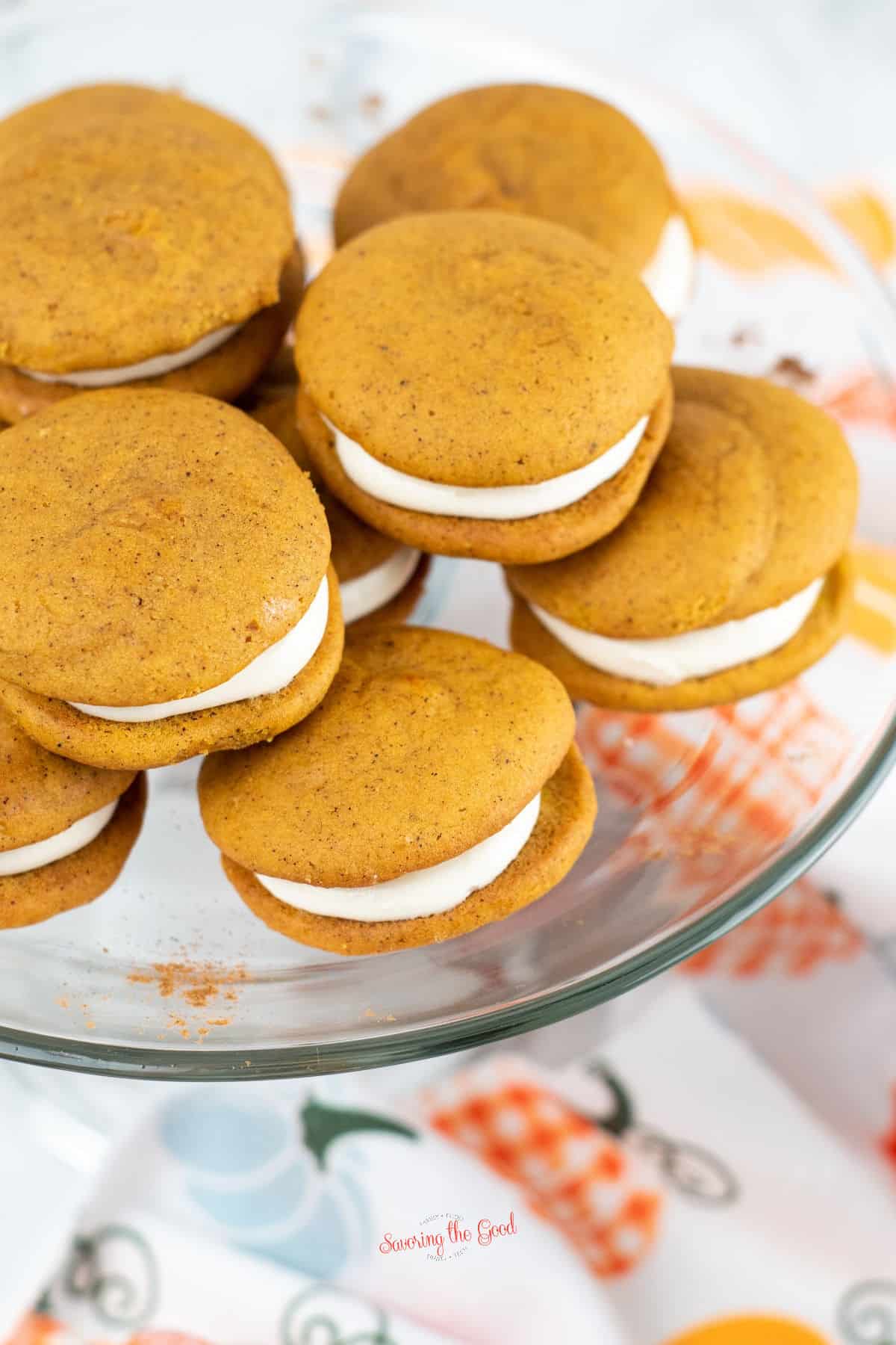 vertical image of a stack of pumpkin whoppie pies on a clear glass serving platter.