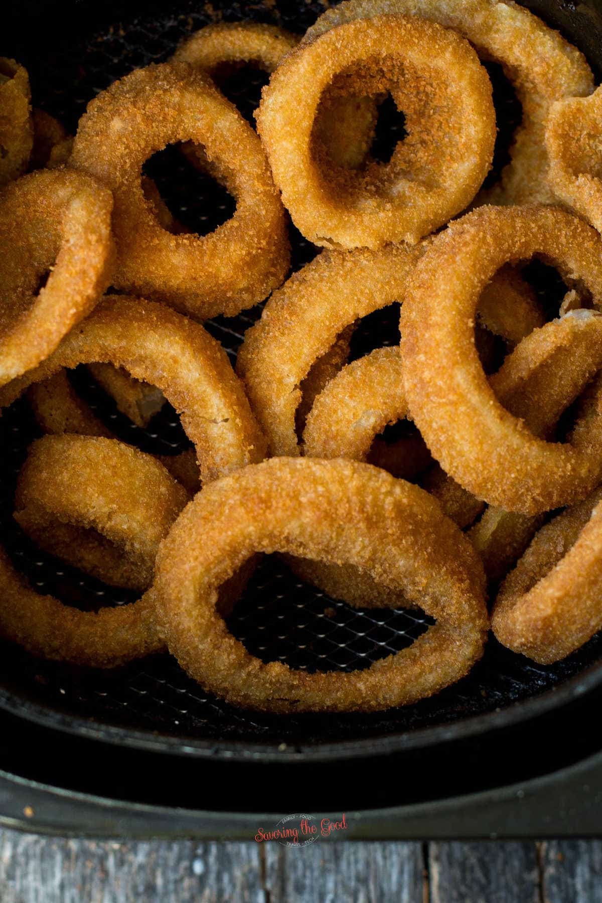vertical image of air fried onion rings in an air fryer basket.