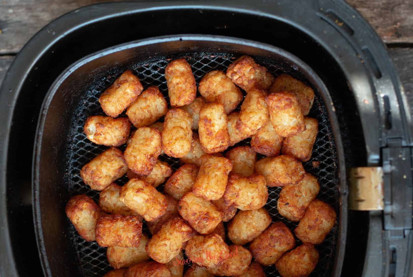 vertical image of cooked tater tots in an air fryer basket.