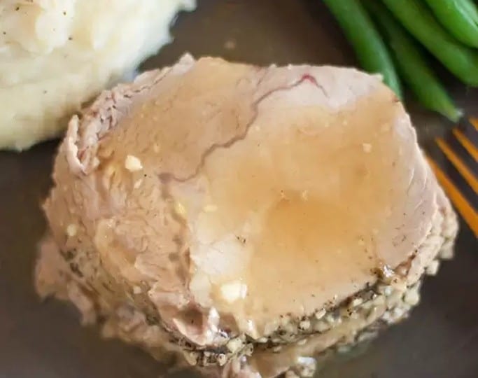 A plate featuring a succulent slice of pork loin, rich with savory sauce, accompanies creamy mashed potatoes and fresh green beans.