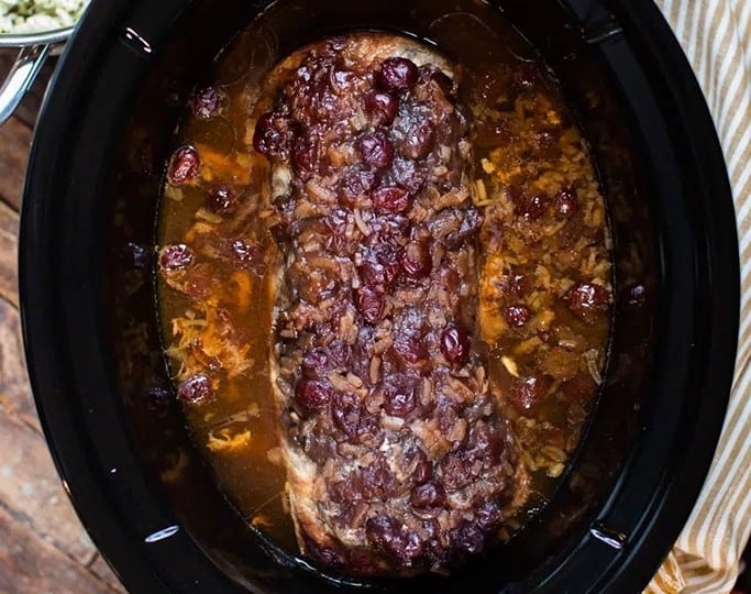 A slow cooker crafts a tender pork loin topped with a rich sauce, surrounded by a bowl of rice and green beans.