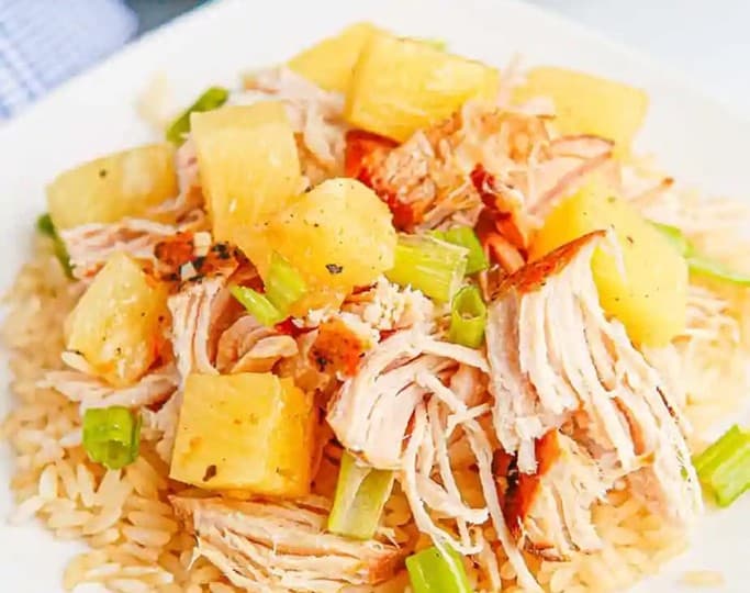 A plate of rice topped with shredded chicken, pineapple chunks, and green onions delivers mouthwatering flavor, reminiscent of pork loin crockpot recipes.