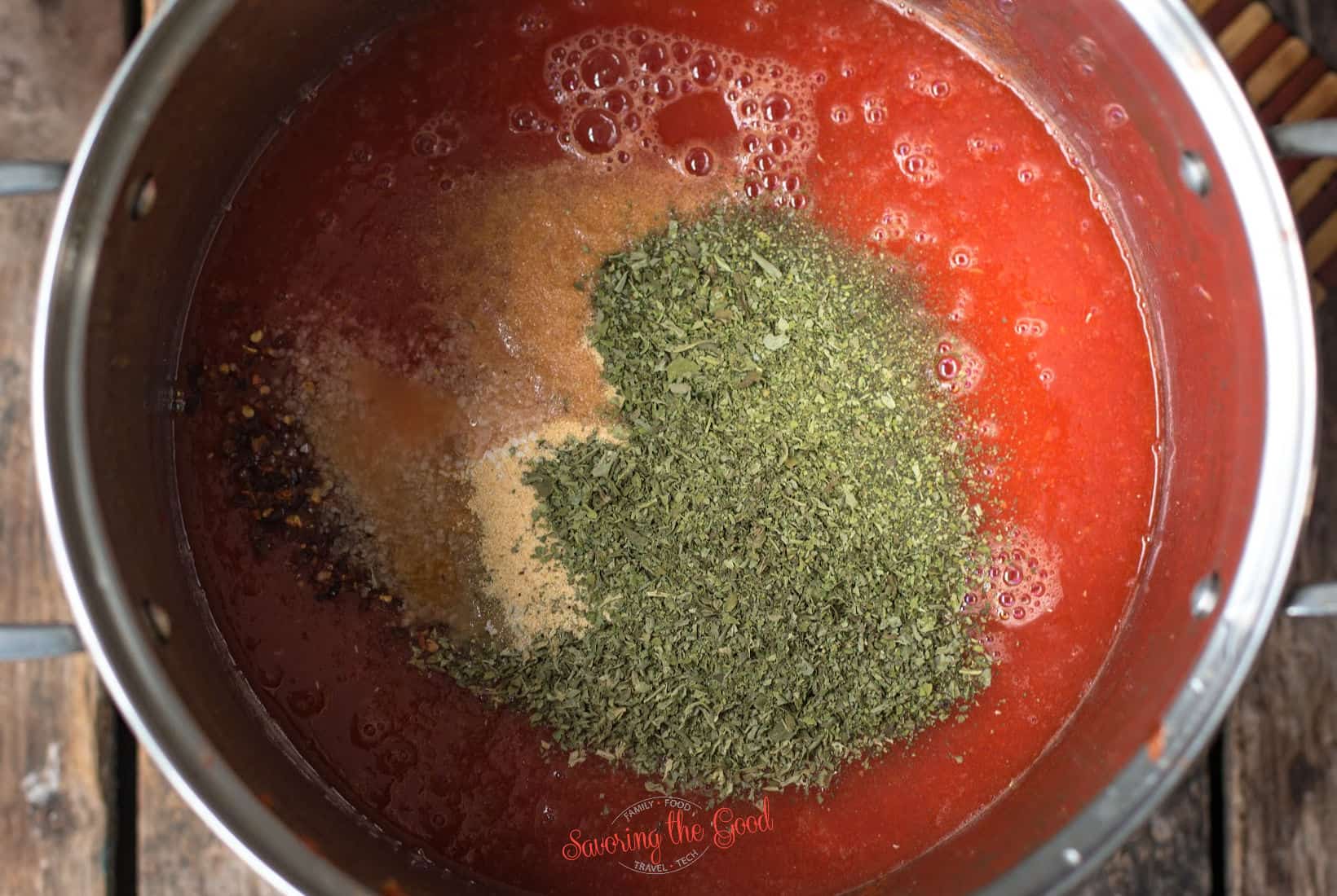 spices in a pot of cooked tomatoes for sauce.