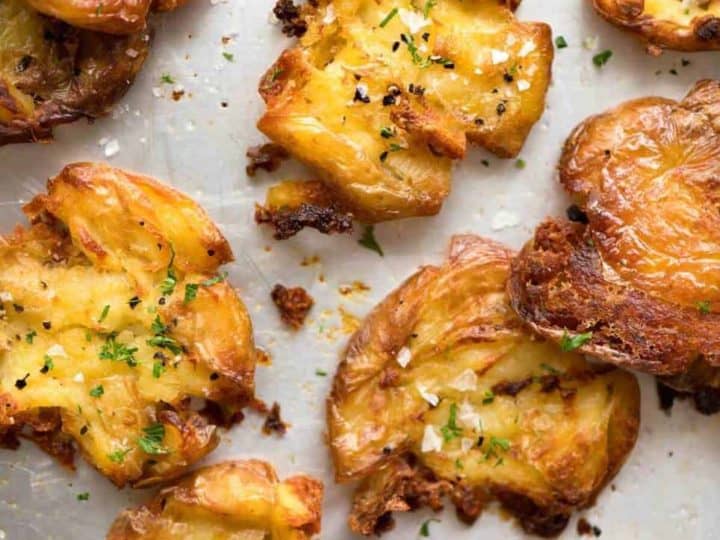 Golden-brown crispy smashed baby potatoes recipes, garnished with chopped herbs and sea salt on a baking sheet.
