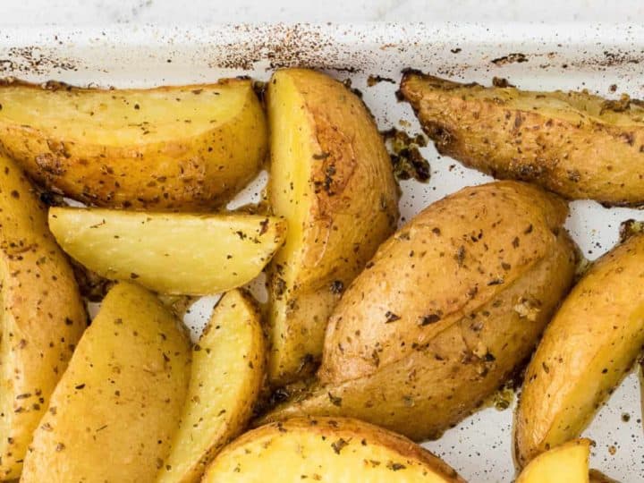 Roasted baby potato wedges seasoned with herbs in a white baking dish.