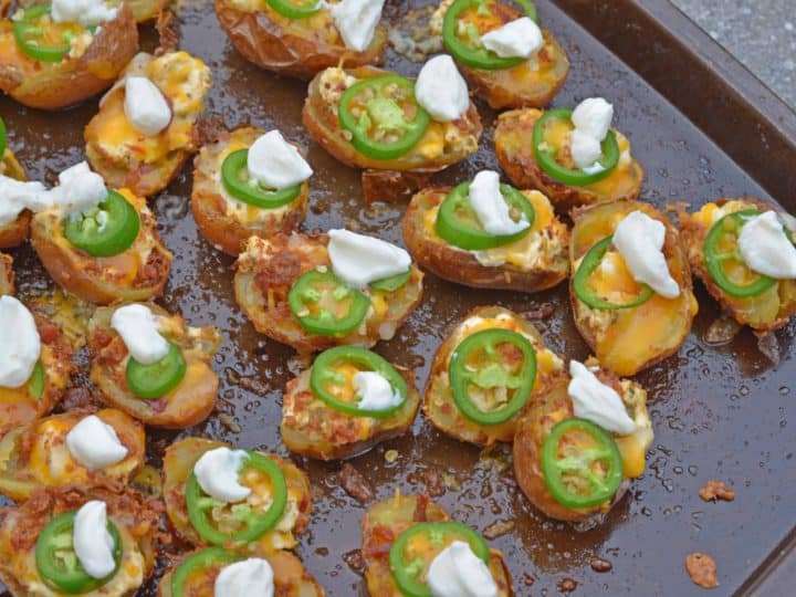 Baked baby potato slices topped with cheese, jalapeño slices, and dollops of sour cream on a baking sheet.