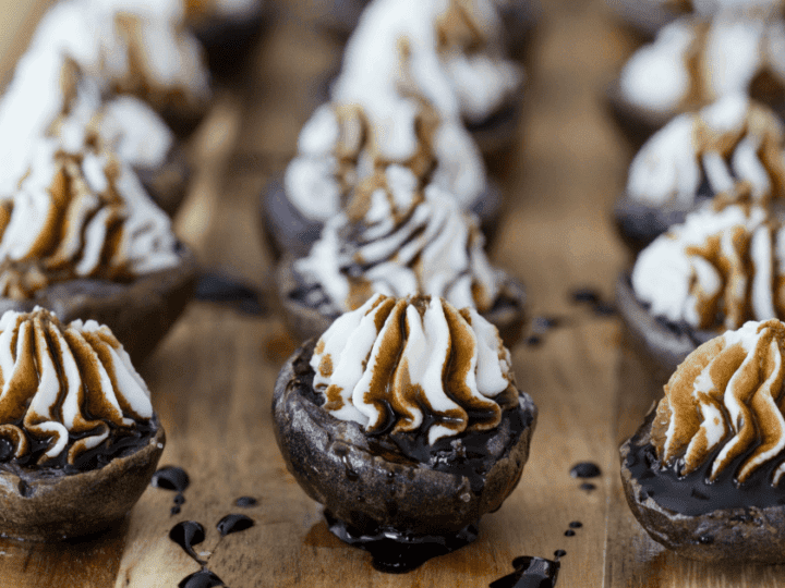 Close-up of chocolate dessert cups topped with whipped cream and caramel sauce, arranged in rows on a wooden board, reminiscent of the meticulous arrangement found in baby potatoes recipes.
