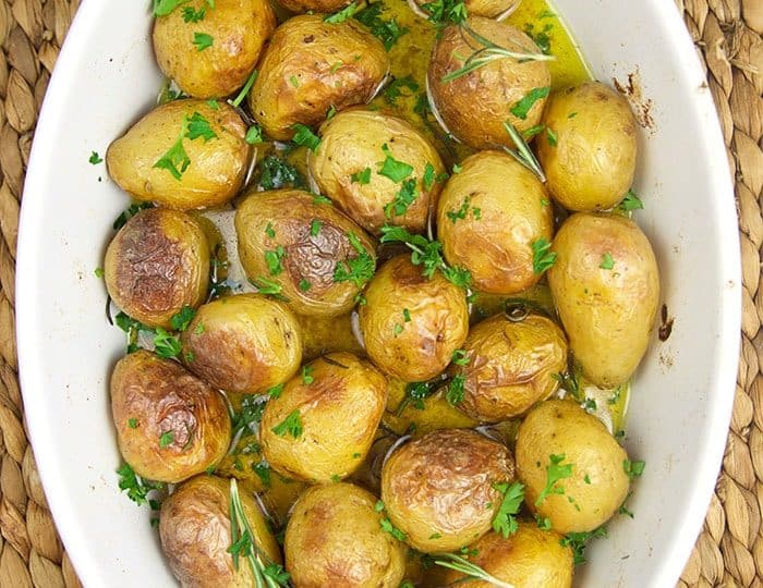 A white oval dish filled with roasted baby potatoes, a delightful choice from your favorite baby potatoes recipes, garnished with parsley and rosemary.