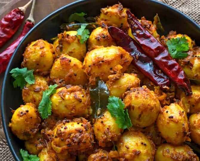A bowl of spiced baby potatoes, a star in many baby potatoes recipes, garnished with dried red chilies and fresh cilantro. Forks are placed alongside.