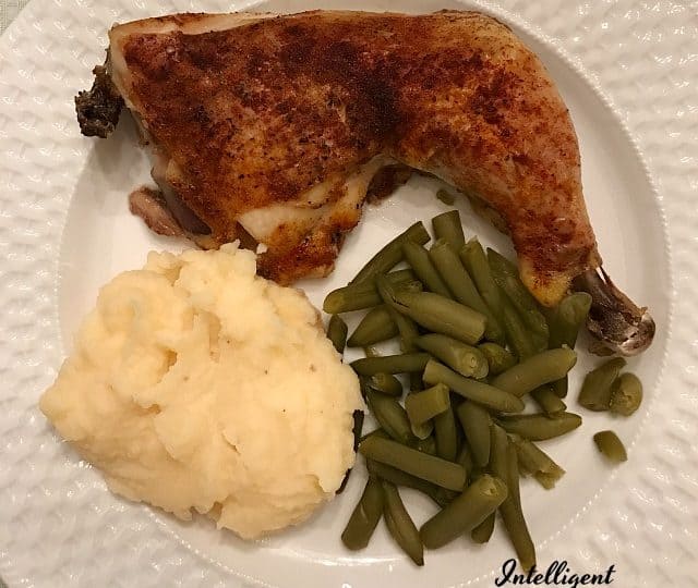 A plate showcases a delicious chicken quarter, roasted to perfection, accompanied by creamy mashed potatoes and vibrant green beans.