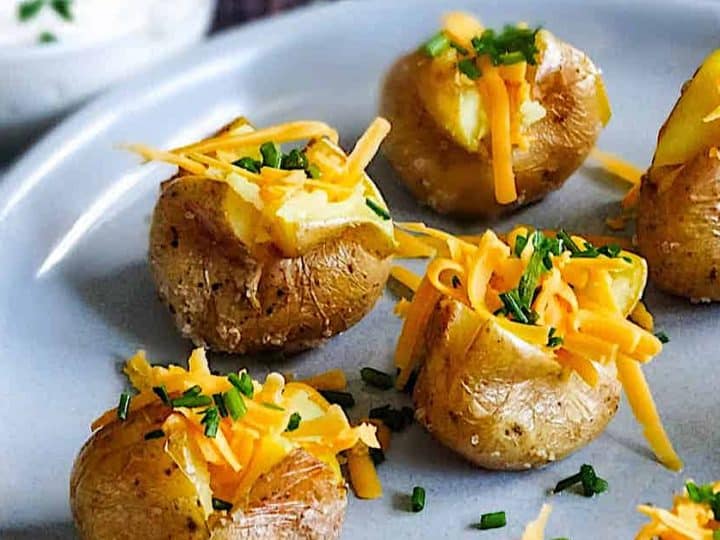 A delicious take on baby potatoes recipes: small baked potatoes topped with melted cheese and chives, served on a plate with a bowl of sour cream in the background.