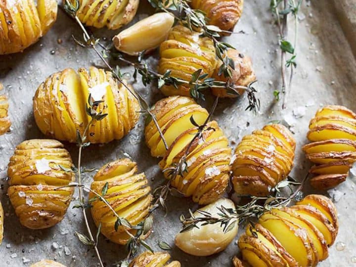 Sliced roasted baby potatoes with garlic cloves and thyme sprigs on a baking tray.