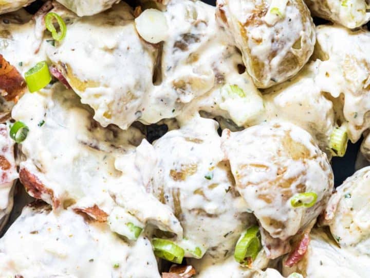 Close-up of a creamy potato salad featuring baby potatoes, crispy bacon, and chopped green onions.