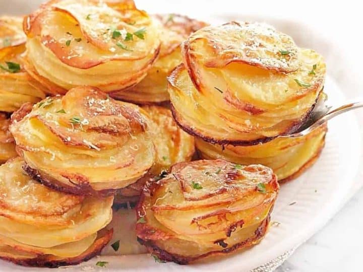A plate of stacked potato gratins, crafted from tender baby potatoes, is elegantly topped with a sprinkle of fresh parsley.