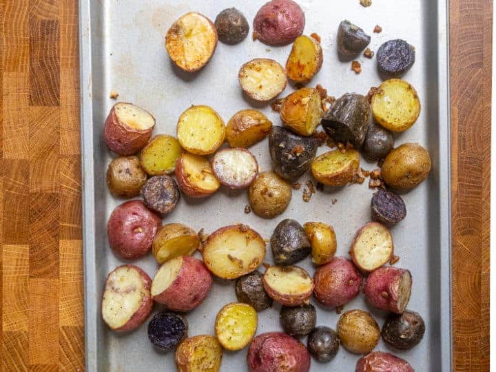 A baking sheet with assorted roasted baby potatoes, showcasing delicious recipes, sits on a wooden surface.