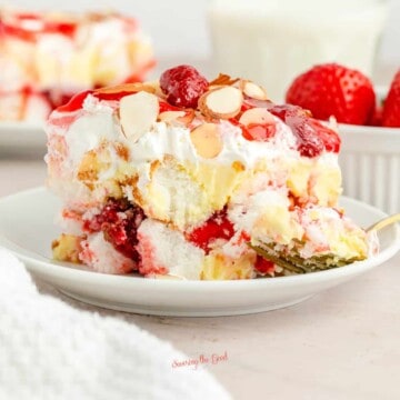 Heaven On Earth Cake (Strawberry Recipe) slice on a small white plate, gold colored fork holding a bite.