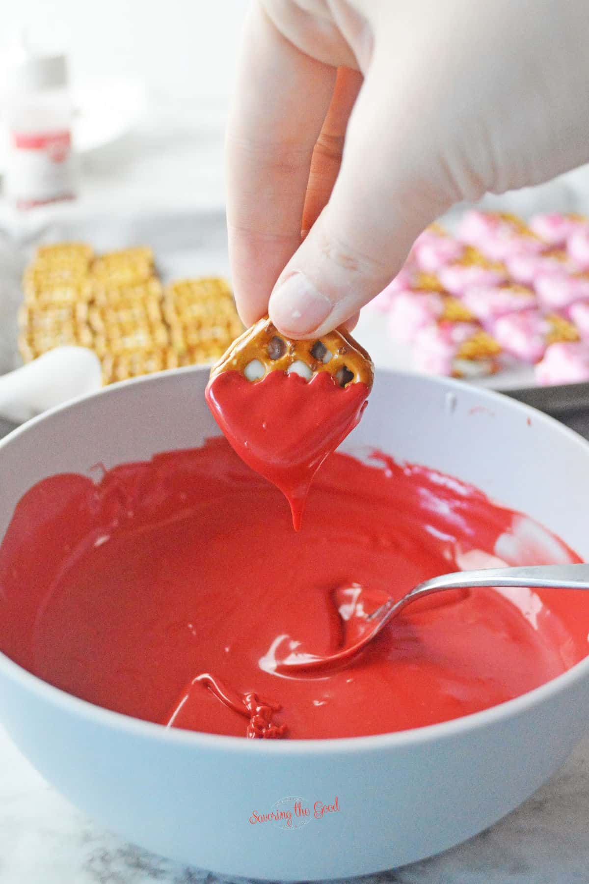 hand dipping a pretzel in red chocolate metls.