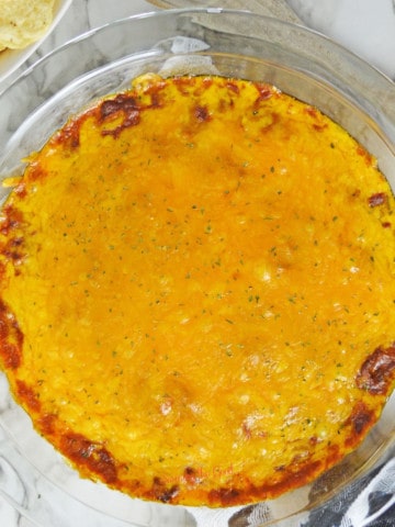 Hormel chili cheese dip in a glass pie plate with chips to the side on a marble like surface.