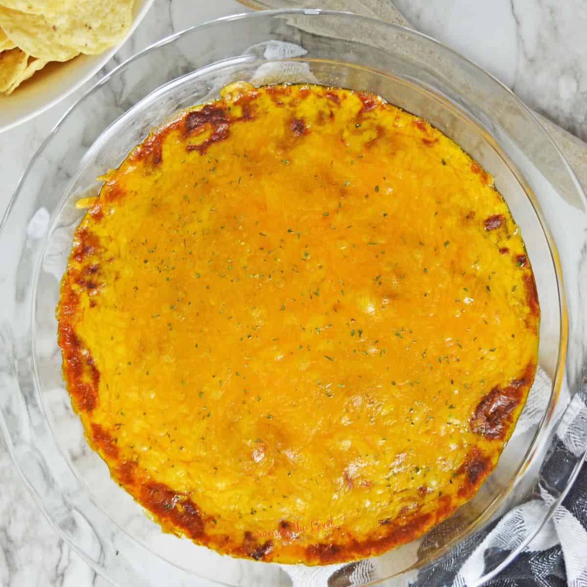 Hormel chili cheese dip in a glass pie plate with chips to the side on a marble like surface.