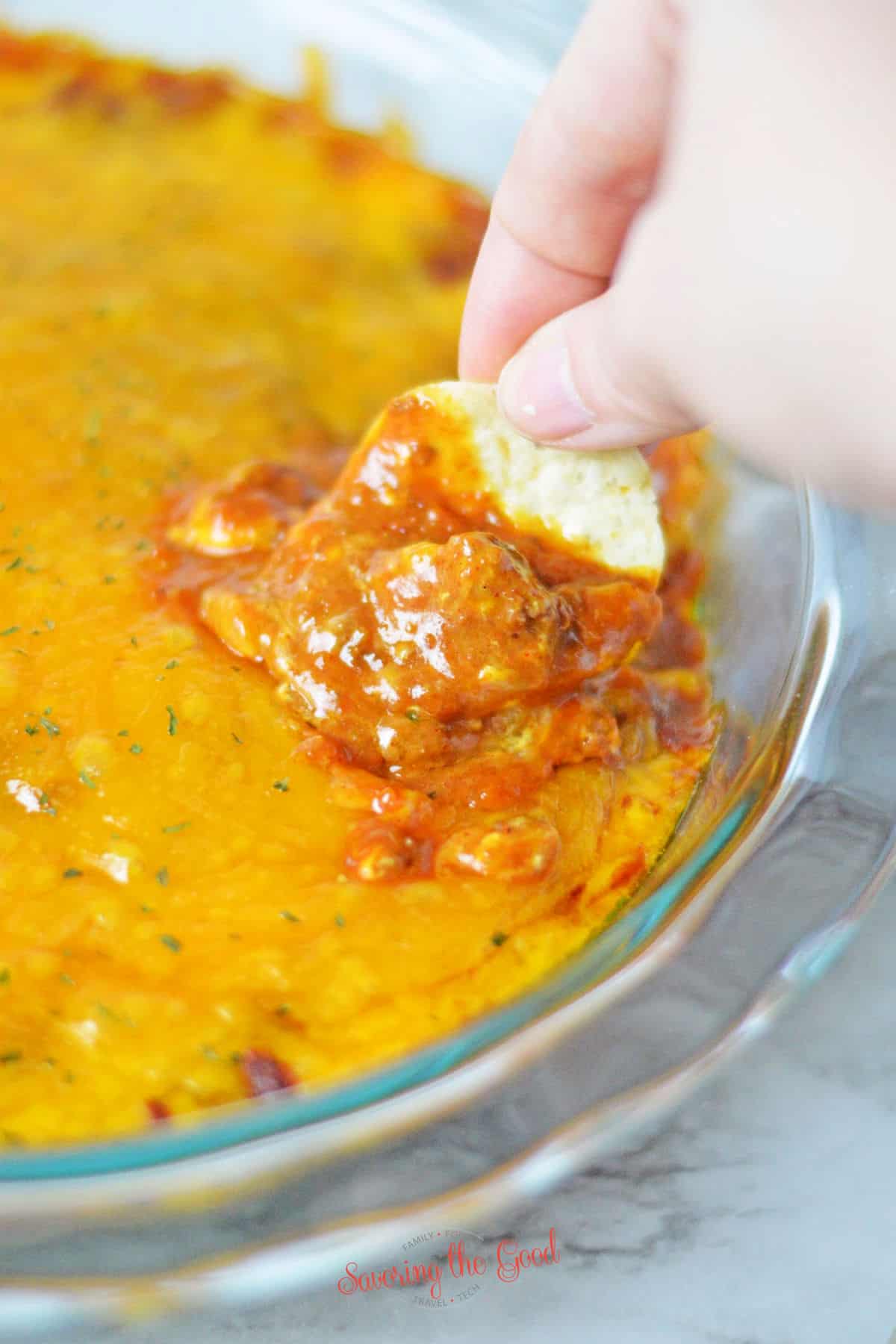hand scooping a portion of chili cheese dip out of a glass pan.