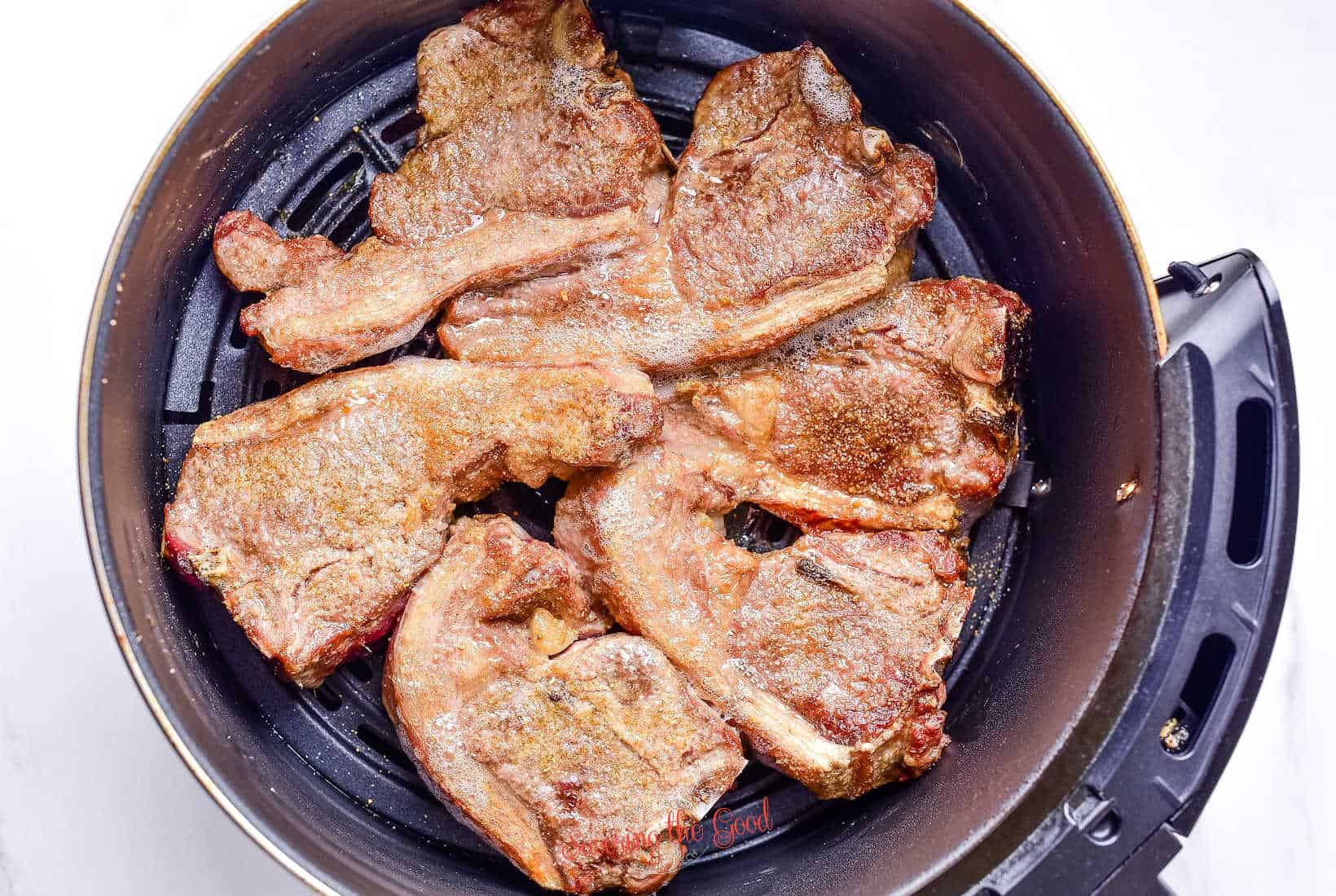 lamb chops in the basket of an air fryer basket starting to cook.