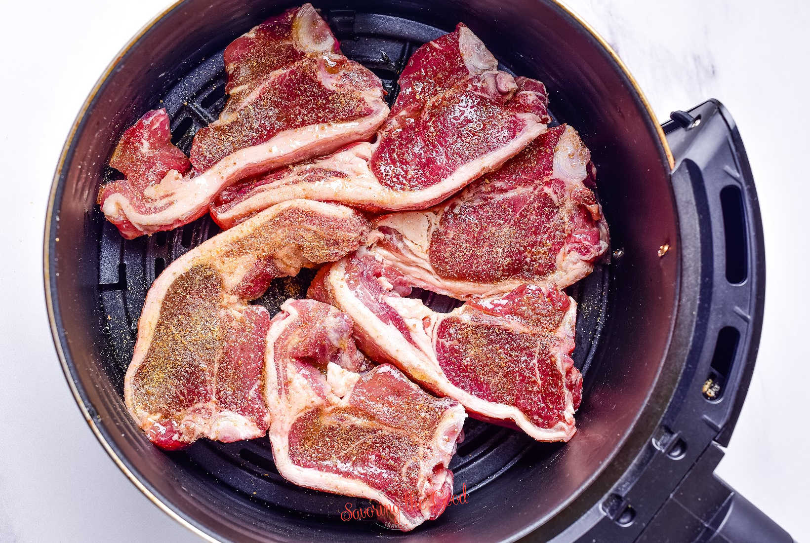 seasoned lamb chops in an air fryer basket, raw, ready to be cooked.