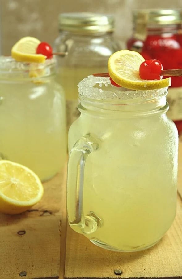 Two mason jars filled with homemade moonshine lemonade and cherries.