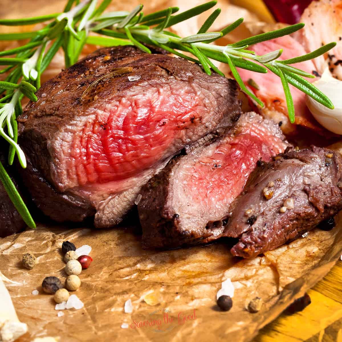 venison sliced on a cutting board with rosemary and whole peppercorn garnish.