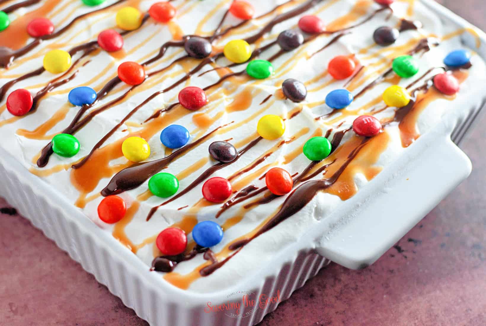 horizontal image, tight shot of a completed ice cream bar cake with garnishes in a white 9x13 pan.