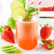 A glass of strawberry lime juice with a striped straw, garnished with lime slices and mint leaves. Fresh strawberries and lime slices are arranged beside the glass, reminiscent of a delightful Strawberry Agua Fresca Recipe.