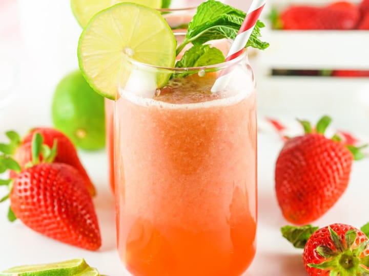 A glass of strawberry lime juice with a striped straw, garnished with lime slices and mint leaves. Fresh strawberries and lime slices are arranged beside the glass, reminiscent of a delightful Strawberry Agua Fresca Recipe.
