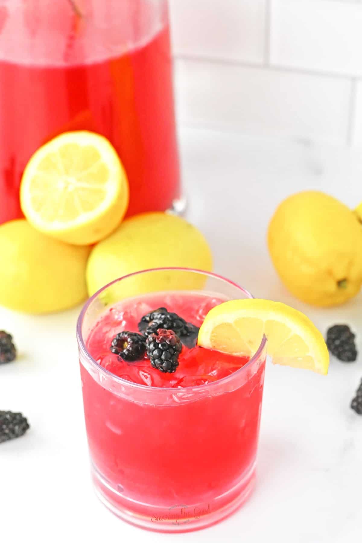 blackberry lemonade in a glass with a pitcher in the background.