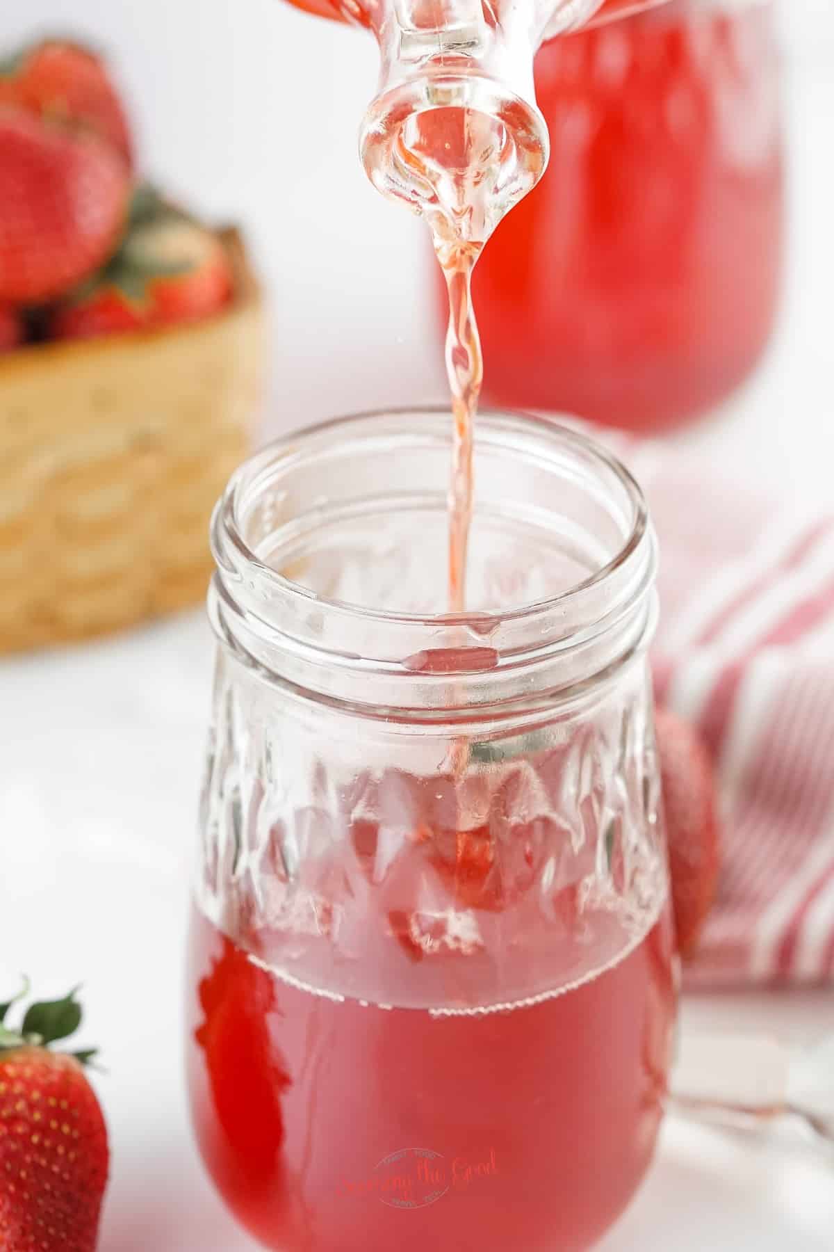 strawberry simple syrup being poured into a clear glass container.