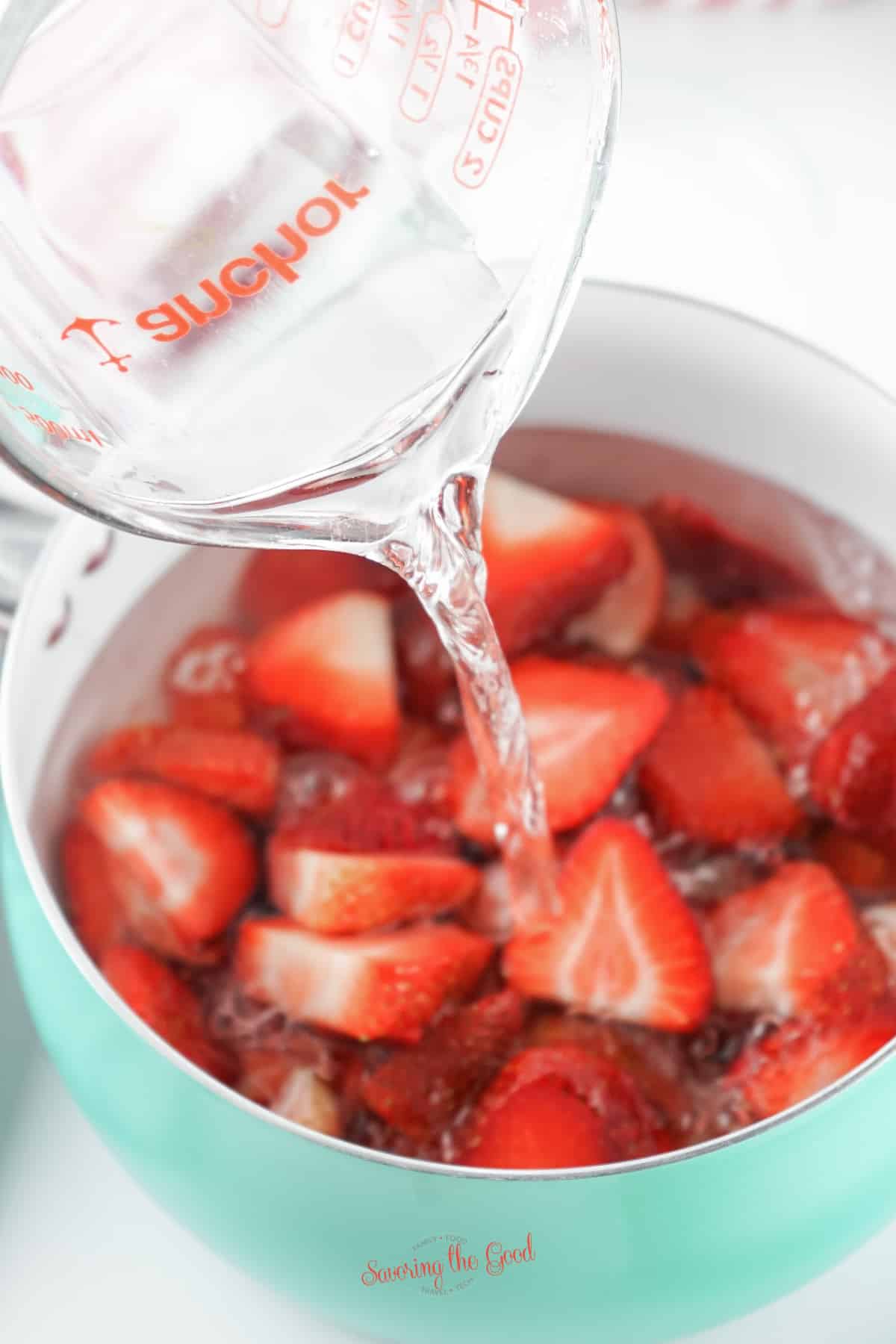 water being poured into a pan with strawberries and suager to make Strawberry Simple Syrup.
