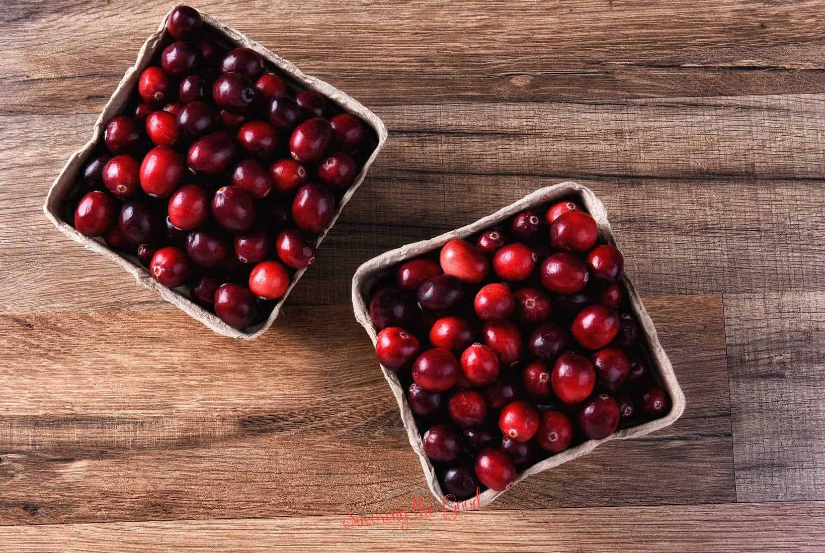 Two baskets of cranberries on a wooden table.