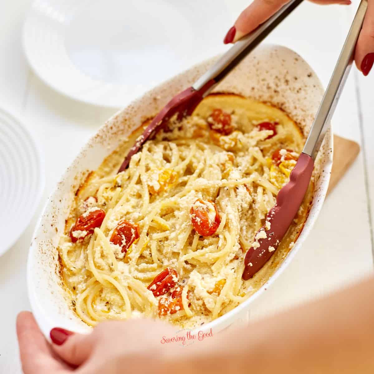 A person is holding a dish of pasta with tomatoes and boursin cheese.