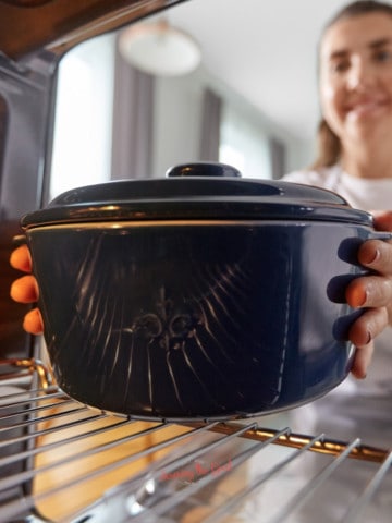 A woman is holding a blue pot in an oven.