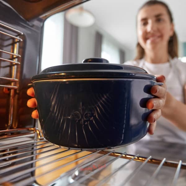 A woman is holding a blue pot in an oven.