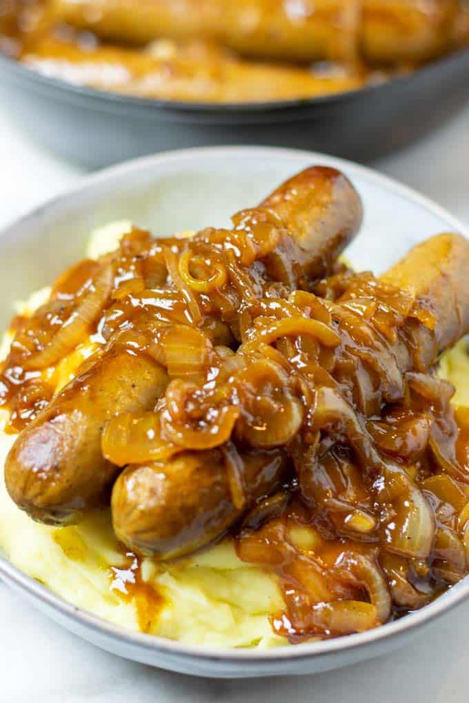 A plate of sausages with onions and mashed potatoes.