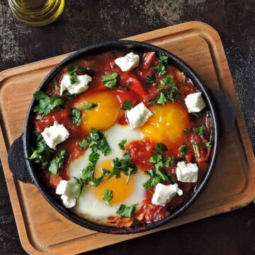 A Moroccan breakfast with eggs and tomatoes served on a wooden cutting board.