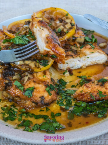 A plate with chicken piccata with lemons and herbs.