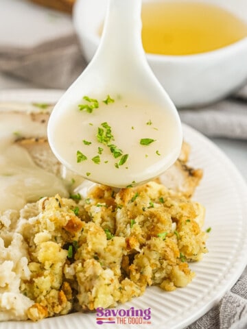 A spoon is pouring turkey gravy with drippings over a plate of mashed potatoes and stuffing.